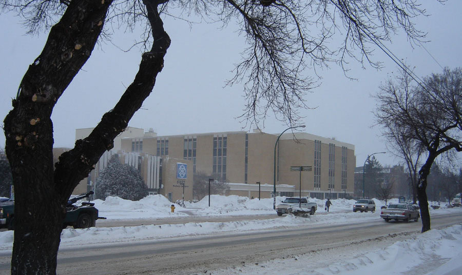 A multistorey golden brick building on the side of a quiet, snowy road.