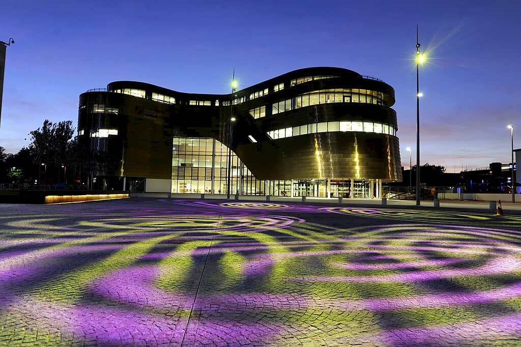 A postmodern university building, framed by a large promenade lit by yellow and purple lights at night. (The Curve building, Teesside University)