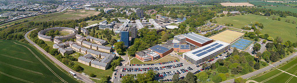 An aerial view of campus buildings, parks, and residences, surrounded by green fields. (University of Essex, Colchester Campus)