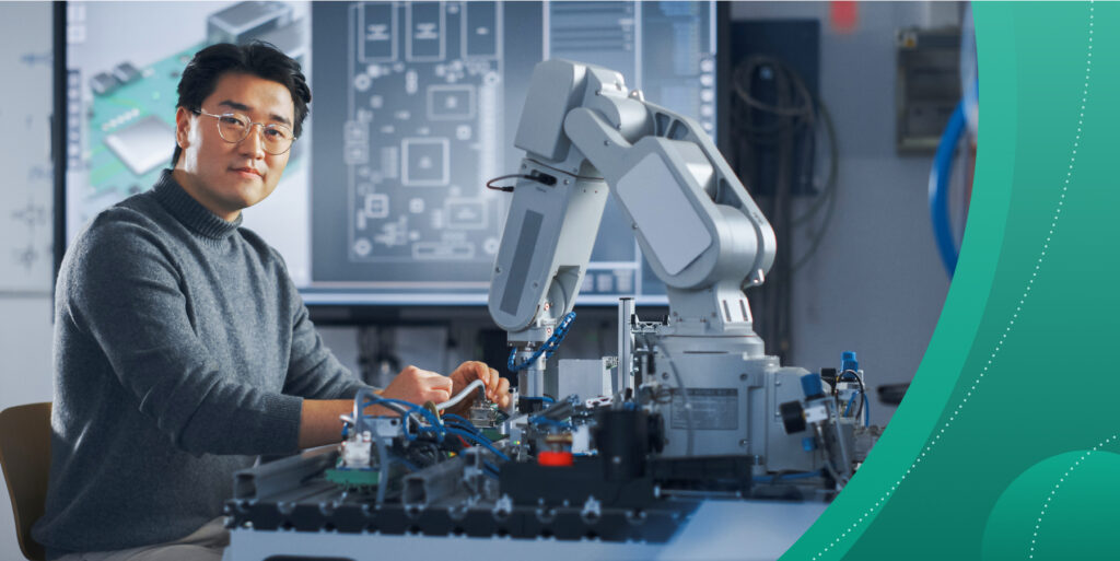 An Asian man works in a technology lab with a complex, armed robotic device.