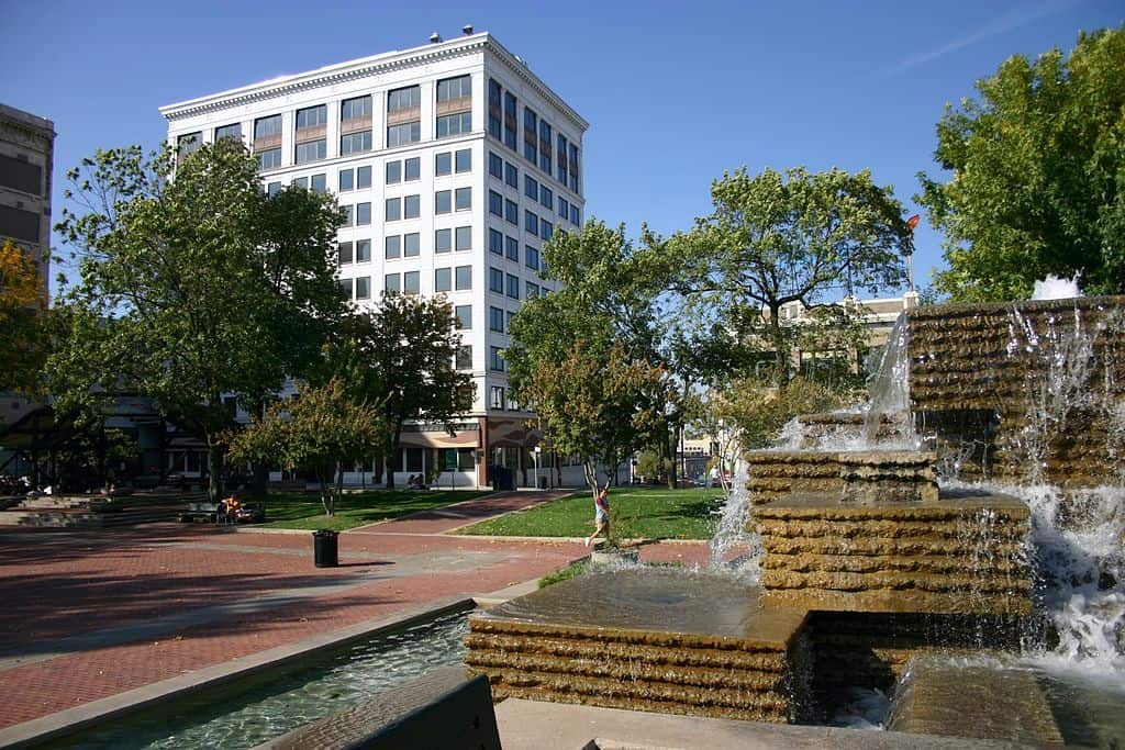 A central city square with tall office buildings, leafy trees, and brick paths and fountains. (Park Square in Springfield, Missouri)